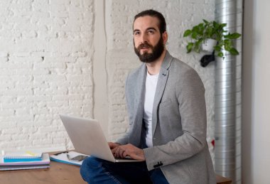 Başarılı hipster girişimci onun modern stüdyo ev ofisinde dizüstü bilgisayar üzerinde çalışıyor. Kendi iş başarısı ile mutlu ve kendinden emin görünümlü. In People başlangıç ve başarılı genç işadamları kavramı.