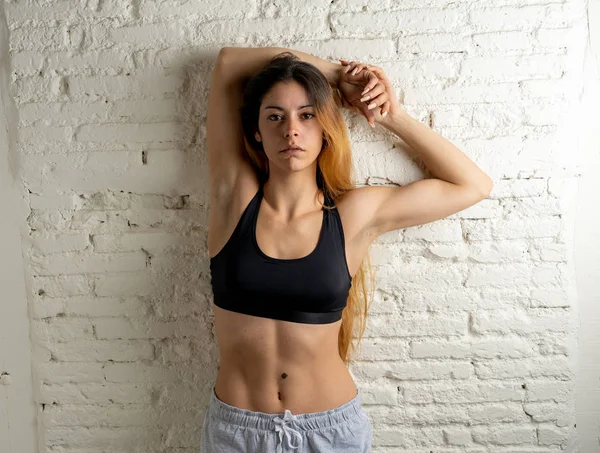 Attractive fitness woman wearing gym top and pants looking sensual and fit. Studio shot of strong woman in sportswear looking healthy against brick wall. In female trained Body and health care.