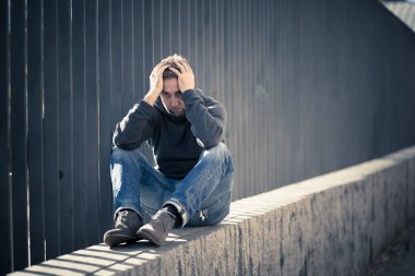 Genç çekici adam acı depresyon stres tek başına oturmak ve üzücü duygu endişeli ve işsizlik ruh sağlığı uyuşturucu ve alkol bağımlılığı kavram yalnız sokakta.