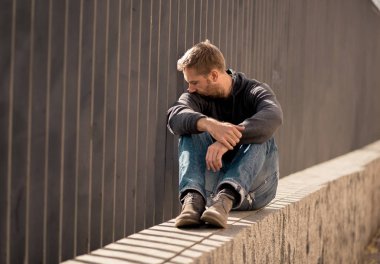 Genç çekici adam acı depresyon stres tek başına oturmak ve üzücü duygu endişeli ve işsizlik ruh sağlığı uyuşturucu ve alkol bağımlılığı kavram yalnız sokakta.