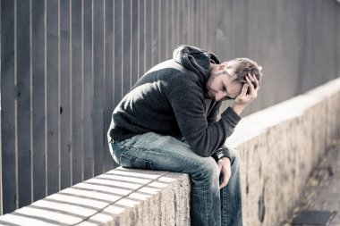 Genç çekici adam acı depresyon stres tek başına oturmak ve üzücü duygu endişeli ve işsizlik ruh sağlığı uyuşturucu ve alkol bağımlılığı kavram yalnız sokakta.