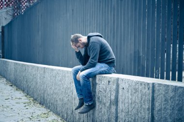 Genç çekici adam acı depresyon stres tek başına oturmak ve üzücü duygu endişeli ve işsizlik ruh sağlığı uyuşturucu ve alkol bağımlılığı kavram yalnız sokakta.