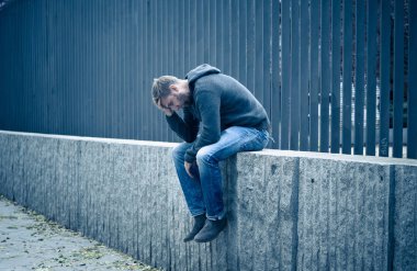 Genç çekici adam acı depresyon stres tek başına oturmak ve üzücü duygu endişeli ve işsizlik ruh sağlığı uyuşturucu ve alkol bağımlılığı kavram yalnız sokakta.