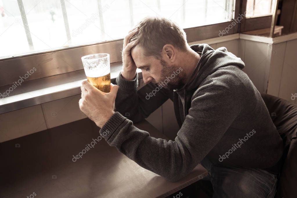 Portrait of a attractive caucasian man drinking beer in a bar pub feeling depressed unhappy and lonely in Alcohol Use Abuse Depression and mental health concept.