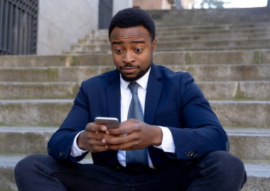 Mutlu Afrika kökenli Amerikalı işadamı cep telefonuna metin iletileri sosyal ağ insanlar, teknoloji online bağlantısı ve girişimci yaratıcı iş kavramı dışında şehir merdivenlerde oturan kontrol.