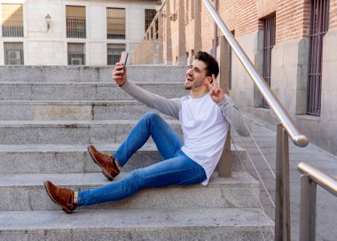 Trendy genç adam akıllı cep telefonunda tatil günlerinde Avrupa şehri sokak veya üniversite kampüs dışında bir selfie alarak heyecanlı. Bayram ve teknoloji, bağlantı ve sosyal medya kavramı.