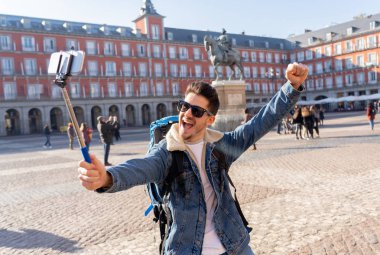 Çekici genç beyaz turistik öğrenci adam mutlu ve heyecanlı bir selfie akıllı cep telefonu ile Plaza Mayor, Madrid, İspanya alarak eğleniyor. Seyahat, tatil, tatil Europe kavramı çevresinde.
