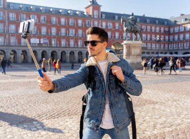 Çekici genç beyaz turistik öğrenci adam mutlu ve heyecanlı bir selfie akıllı cep telefonu ile Plaza Mayor, Madrid, İspanya alarak eğleniyor. Seyahat, tatil, tatil Europe kavramı çevresinde.
