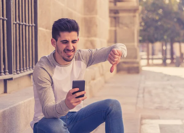 Portrait of young student man reacting negative to post in social media network or dating app with dislike showing thumb down. In social network rating likes, reactions and reassurance youth problems.