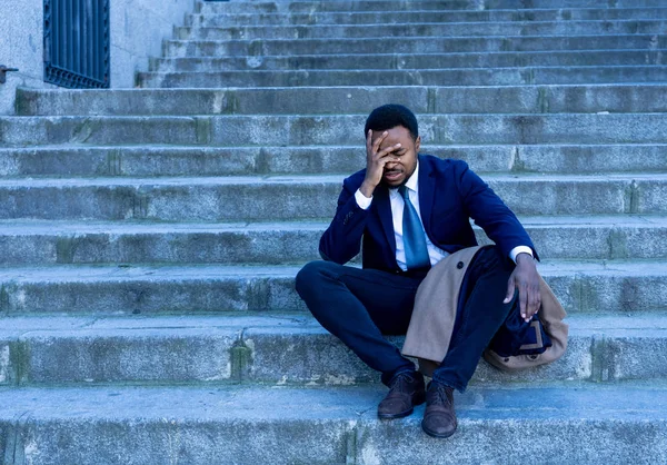 Young fired african american business man lost in depression crying sitting on ground street stairs suffering emotional pain sadness in grunge lighting. Unemployment, Depression and people concept.