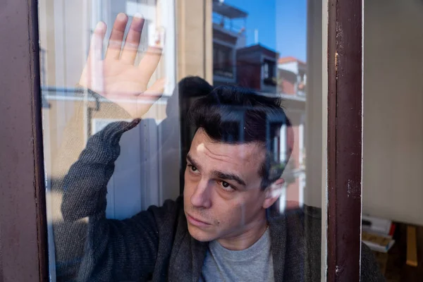 Close up portrait of young sad unhappy caucasian man looking worried, desperate and suicidal through the window at home. feeling worthless and in pain. In People, Depression and crisis concept.