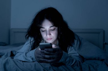 Sohbet ve akıllı telefonunu uykulu, bıkkın ve yorgun gece geç saatlerde kullanarak internette sörf bağımlısı genç kadın. Dramatik koyu. Internet, mobil bağımlılığı ve uykusuzluk kavramı.