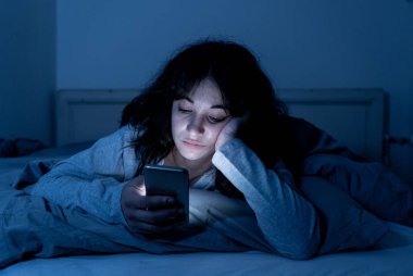 Sohbet ve akıllı telefonunu uykulu, bıkkın ve yorgun gece geç saatlerde kullanarak internette sörf bağımlısı genç kadın. Dramatik koyu. Internet, mobil bağımlılığı ve uykusuzluk kavramı.