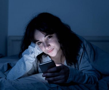 Sohbet ve akıllı telefonunu uykulu, bıkkın ve yorgun gece geç saatlerde kullanarak internette sörf bağımlısı genç kadın. Dramatik koyu. Internet, mobil bağımlılığı ve uykusuzluk kavramı.