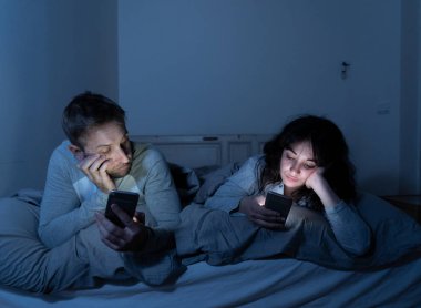 Akıllı telefonlarda geceleri yatakta genç sıkılmış çift portresi yaşam tarzı Oyunlar, sosyal medya, birbirimizi görmezden apps ile takıntılı. İlişki iletişim sorunları ve telefonu bağımlılığı konsepti.