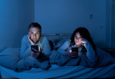Akıllı telefonlarda geceleri yatakta genç sıkılmış çift portresi yaşam tarzı Oyunlar, sosyal medya, birbirimizi görmezden apps ile takıntılı. İlişki iletişim sorunları ve telefonu bağımlılığı konsepti.