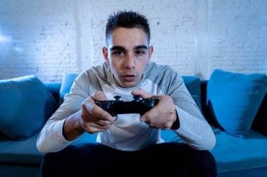 Ucube yoğun bağımlısı yüz erkek oyun bağımlılığı konsol oyun istasyonu ve video having oyunculuk ile kablosuz uzaktan joystick kullanarak gece video oyunları oynarken genç öğrenci adam portresi.