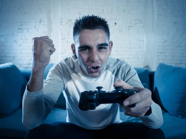 Portrait of young man having fun playing video games using wireless remote joystick with freak intense happy face celebrating winning. In Male game addiction to console play station and video.