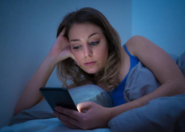 中毒若い美しい女性ベッド チャット 携帯中毒と技術乱用概念で夜遅く眠そうな 疲れている彼女のスマート フォンを使用してインターネット上でサーフィン — ストック写真