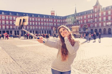 Güzel genç kadın mutlu ve heyecanlı Plaza Mayor Madrid İspanya alarak selfie veya video tarihi mimari zevk onun takipçileri için poz selfie sopa ile. Turizm ve seyahat Europe.