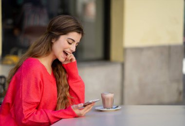 Neşeli ve mutlu akıllı telefon app sosyal medya kentsel şehirde kahve yudumlarken sohbet arayan genç ve güzel moda kadın. Yaşam tarzı mobil kullanım ve online app ve teknoloji kavramı.