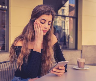 Genç ve güzel kadın şık siyah top ile seyir sıkılmış kahve içme, kahve dükkanında dışında akıllı telefon iletileri gönderme. Yorgun ve donuk duygu. Yaşam tarzı ve teknoloji kavram kullanmak.