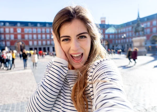 Beautiful student tourist woman happy and excited taking close up selfie in Plaza Mayor Madrid Looking cheerful and joyful having fun. In tourism, travel around europe and posting online adventures.