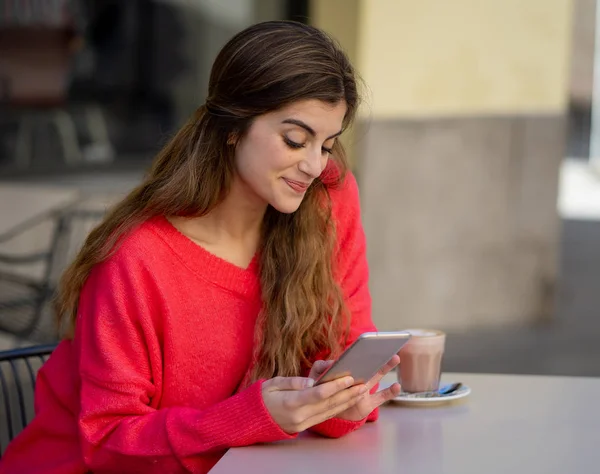 Pretty Happy young woman chatting and using smart mobile phone app looking cheerful drinking coffee in a urban coffee terrace. In online dating, mobile app, internet, connections and technology use.