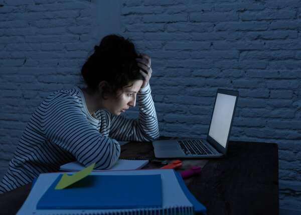 Переутомленная и уставшая студентка работает допоздна за своим ноутбуком, стараясь не заснуть, чувствуя усталость, беспокойство и грусть. Мрачный темный свет. Концепция онлайн обучения и работы со стрессом
.