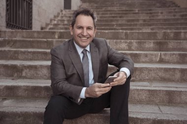 Akıllı telefon e-posta ve sosyal medya şehir merdivenlerde kontrol üzerinde mutlu orta yaşlı işadamı. İnsanlar, yeni teknoloji, online bağlantı ve girişimci yaratıcı iş mobil iletişim kavramı.