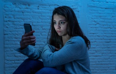 Gece katta üzgün korkmuş genç kadın portre vurguladı ve akıllı cep telefonu tehdit siber zorbalık taciz muzdarip. Stalker tarafından istismar online olmak umutsuz ve depresif.