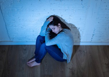 Genç umutsuz Latin kadının portresi, kopya alanı ve Moody ışık ile beyaz bir duvara karşı yerde oturan, mutsuz, yalnız, umutsuz ve üzücü hissediyor. Depresyon ve zihinsel sağlık konsepti.