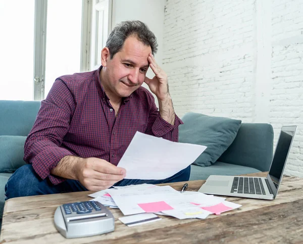 Mature attractive man on computer looking stressed and worried with credit card payments and home finances accounting costs charges taxes and mortgage in paying bills financial problems and debts.