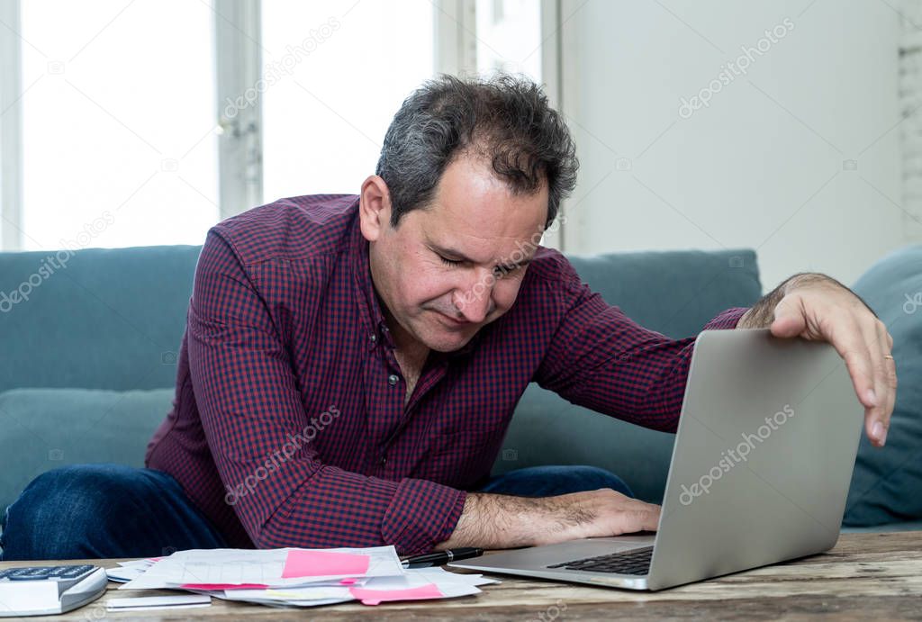 Mature attractive man on computer looking stressed and worried with credit card payments and home finances accounting costs charges taxes and mortgage in paying bills financial problems and debts.