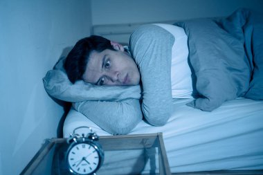 Uykusuz ve çaresiz genç beyaz adam Uykusuz geceleri uyku mümkün değil, hayal kırıklığına ve stres ve uyku bozukluğu kavramı uykusuzluk muzdarip saat bakıyor endişeli.