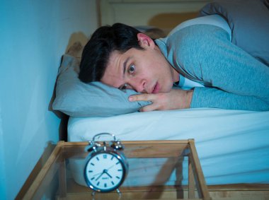 Uykusuz ve çaresiz genç beyaz adam Uykusuz geceleri uyku mümkün değil, hayal kırıklığına ve stres ve uyku bozukluğu kavramı uykusuzluk muzdarip saat bakıyor endişeli.