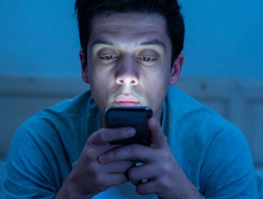 Addicted Man sohbet ve yatakta gece geç saatlere kadar akıllı telefon ile Internette sörf. Sıkılmış, uykusuz ve kasvetli ışık ile karanlık odada yorgun. Uykusuzluk ve mobil bağımlılık kavramı.