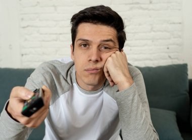 Film veya canlı spor için uzaktan kumanda zap ile kanepede genç sıkılmış adamın Lifestyle portre. İlgilendiğim bira içmeye bakıyor. Sedanter ve kitle sosyal medya veya televizyon bağımlılığı.