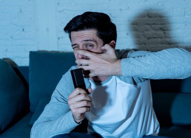TV izlerken ve uzaktan kumanda tutarak korku, anksiyete jestleri yapma korkmuş ve şok hissi genç adam yaşam tarzı portre. Şiddet ve korku filmleri ve serisi internet akışı.