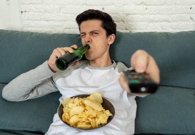 Genç adam TV şovları ya da filmler ile nefreti hissi sevmediğim kanallar anahtarlama. Bira içerken, onaylamadan bir bakış. Çöp ve kötü televizyon gösterileri ve sağlıksız yaşam tarzı.