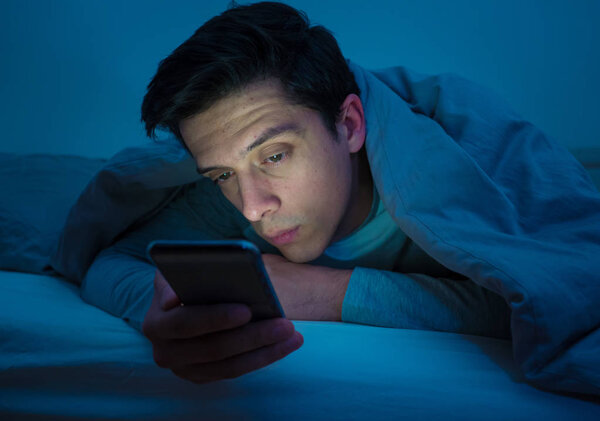 Молодой наркоман по ночам просыпается в постели, используя смартфон для чата, флирта и отправки текстовых сообщений. В области коммуникации, интернет-зависимости и злоупотребления социальными сетями
