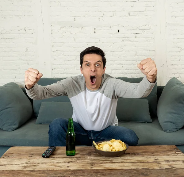 Lifestyle portrait of excited football fan having fun watching soccer or football game on television. Enjoying and celebrating goal and victory drinking beer and eating chips. Sports fans and Goal.