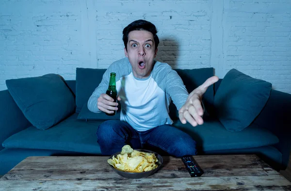 Young man drinking beer at home watching soccer football match or sports game in television at night. Screaming and celebrating goal or victory. In celebration, sports and fans concept.