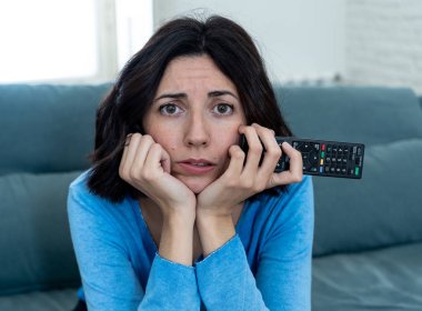 Genç üzgün kadın kanepede kontrol uzaktan zapping kullanarak kötü Tv şovları ve programlama sıkılmış . İlgisiz, ilgisiz ve uykusuz görünüyor. İnsanlar, çok fazla kötü televizyon ve Sedanter yaşam tarzı.
