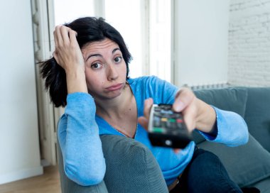 Genç üzgün kadın kanepede kontrol uzaktan zapping kullanarak kötü Tv şovları ve programlama sıkılmış . İlgisiz, ilgisiz ve uykusuz görünüyor. İnsanlar, çok fazla kötü televizyon ve Sedanter yaşam tarzı.