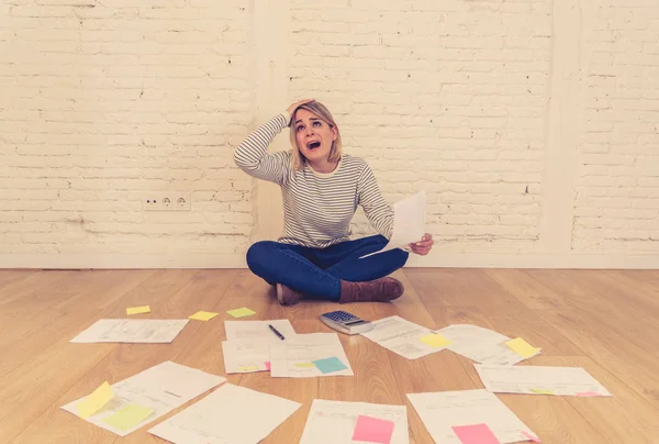 Portrait of worried young woman feeling stressed and desperate on the ground with calculator accounting expenses not able to pay mortgage. In paying debts and domestic bills and financial problems.