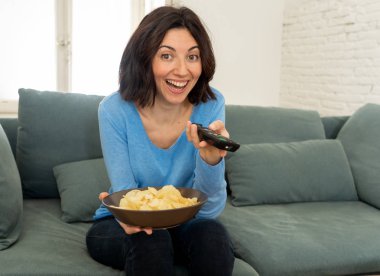 Tv uzaktan kumanda başka bir film veya favori Tv Show için zapping ile kanepede Mutlu kadın. Hevesli görünüyor, onay jestleri yapıyor ve cips yemek. İnsanlarda, teknoloji ve eğlence kavramı.