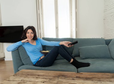 Televizyon kumandalı mutlu kadın TV dizisinin en sevdiği filmini izlemeye hazır. Hevesli görünüyor, onay jestleri yapıyor ve cips yiyor. İnsanlarda, teknoloji ve eğlence kavramı.