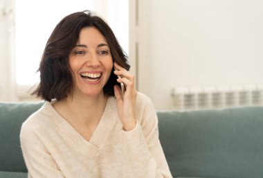 Rahat çekici kadın arkadaşları evde kanepede mutlu gülümseyerek konuşurken Yaşam tarzı portresi. Boş zaman internet, akıllı telefon ve sosyal ağ kavramı.