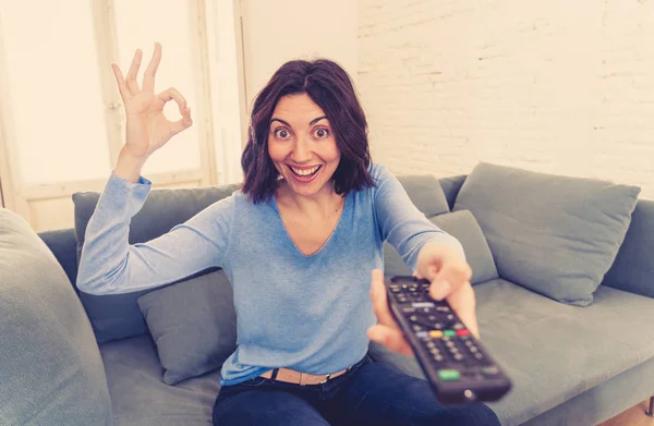 Happy woman on sofa with TV remote control ready to watch favorite movie of TV Show. Looking enthusiastic, making gestures of approval and eating chips. In people, technology and leisure concept.